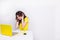 A brunette girl with curly hair looks frustrated sitting in front of laptop in yellow case. She sits behind white table