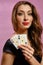 Brunette girl with earring in nose, in black dress. Showing two aces while posing on pink studio background. Poker