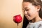 Brunette girl looking with desire at a red candy apple. Orange background