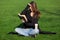 A brunette girl sits in a green meadow and indignantly reads a hardback book.