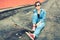 Brunette girl with skateboard sitting, smiling at camera, wearing jeans and modern outfit. Instagram filter, modern concept of