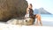 brunette girl in transparent lace frock sits on rock at beach