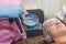 A brunette girl undergoes procedures in a spa salon, a master beautician in blue gloves applies a thick layer of a green mask,