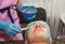 A brunette girl undergoes procedures in a spa salon, a master beautician in blue gloves applies a thick layer of a green mask,