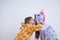Brunette girl in unicorn pajamas stands excited while her brother in giraffa pajamas hugging and kissing her, isolated