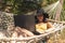 Brunette girl in a yellow swimsuit sitting in a hammock using a laptop, work on vacation, freelance, remote work, online earnings