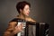 A brunette in a gold shirt, with short haircut, on a light gray background of the Studio. With accordion musician