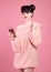 Brunette holding mobile phone. Fashion studio teen look style over pink. Fashionable young girl wears wool sweater posing isolate