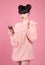 Brunette holding mobile telephone. Fashion studio teen look style over pink. Fashionable young girl wears wool sweater posing iso