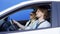 Brunette man and blonde woman are in white car against blue background. Smiling driver is drinking coffee to go and