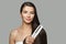 Brunette model woman holding hair iron and straightening her healthy long dark hair on white background. Haircare and hair styling