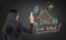 Brunette real estate agent is drawing a new colourful house on the black chalkboard.