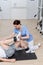 brunette rehabilitologist assisting man working out