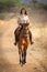 Brunette rides horse on dirt track smiling