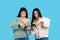 The brunette sisters are amazement looking at the smartphone screen with displeasure. Blue background