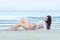 Brunette slim body lady wear bottom bikini and wet white shirt lying back on sand