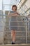 A brunette in a striped dress smiling stands on the stairs