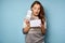 Brunette in with surprise opening her mouth looks in a gift box, standing on a blue background.