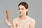 Brunette woman with acne on face holding carrot  on grey