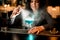 Brunette woman bartender sprinkles on blue alcoholic cocktail in glass on bar counter.