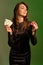 Brunette woman in black dress is smiling, showing two red chips and aces, posing against colorful studio background