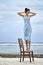Brunette woman in blue dress posing on chair on sand beach