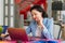 a brunette woman in a blue jacket sits at a desk and works on a laptop.