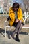 A brunette woman in a bright yellow jacket sat down bench in the park to shake out a stone