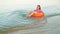 A brunette woman dangles in a swimming circle in the sea near the shore