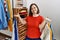 Brunette woman with down syndrome holding hangers with different clothes at retail shop