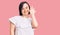 Brunette woman with down syndrome wearing casual white tshirt waiving saying hello happy and smiling, friendly welcome gesture