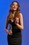 Brunette woman with earring in nose, in black dress. Holding glass of champagne, two red chips, posing on blue