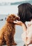 Brunette woman kissing her little pet, redhead dog breed toy poodle outdoors