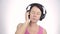 Brunette woman listening music with big headphones and dancing on a light background