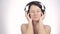 Brunette woman listening music with big headphones and dancing on a light background