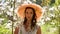 Brunette woman with long hair in a straw hat stands in the apple orchard