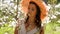 Brunette woman with long hair in a straw hat stands in the apple orchard