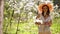 Brunette woman with long hair in a straw hat stands in the apple orchard