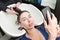 Brunette woman looks at smartphone while hairdresser is busy washing her hair at beauty salon