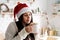 Brunette woman in santa hat holding a cup of marshmallow cocoa in the kitchen