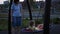 Brunette woman shakes her daughter on swing with net on at dusk in public park