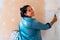 Brunette woman smiling painting a wall on white with a paint roller. Looking at the camera