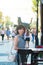 A brunette woman stands near a table of a street cafe in a European city on a busy street