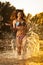 brunette woman in swimsuit running in river water. young woman playing with water during sunset. Beautiful woman