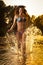 brunette woman in swimsuit running in river water. young woman playing with water during sunset. Beautiful woman
