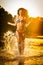 brunette woman in swimsuit running in river water. young woman playing with water during sunset. Beautiful woman