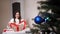 Brunette woman unfolds a gift decorated with a red ribbon next to a christmas tree