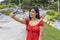 brunette woman wearing red dress using smart phone and taking a selfie at the skate park, smiling