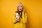 A brunette in a yellow sweater stands on a yellow background with a thermos in hands and looks joyfully into the frame