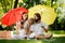 Brunettes parents with two kids have a rest on the lawn under the bright red and yellow umbrellas covering them from the